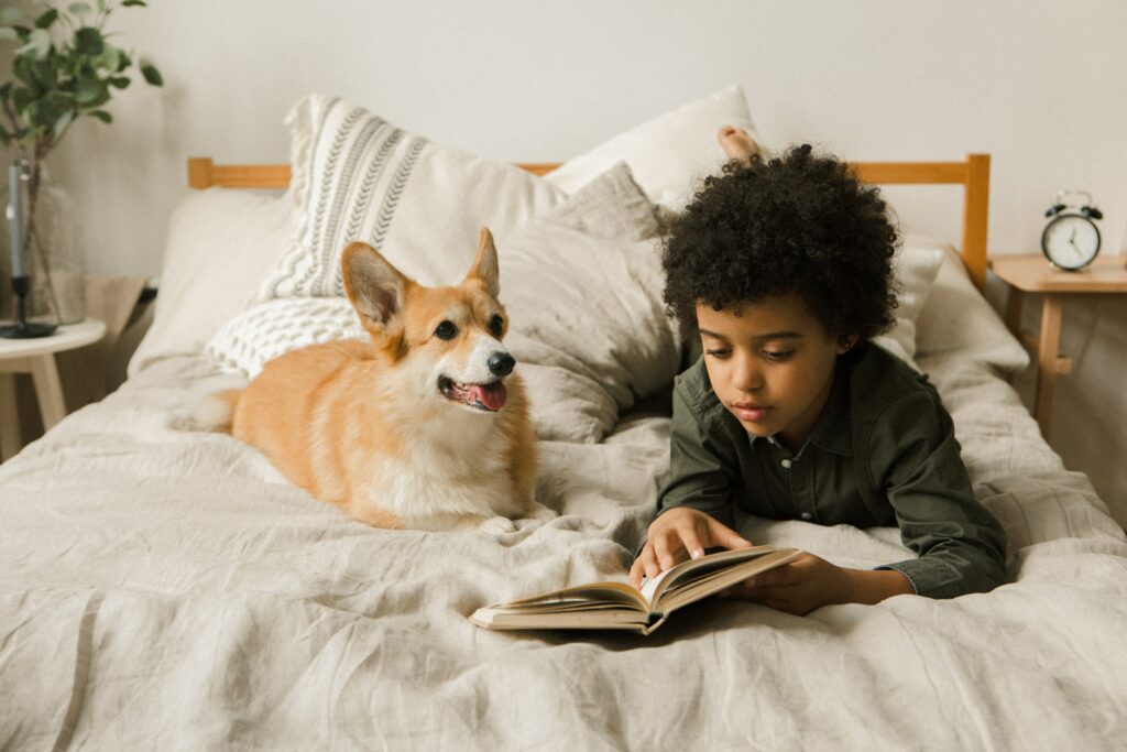 boy and corgi laying on bed reading a book
